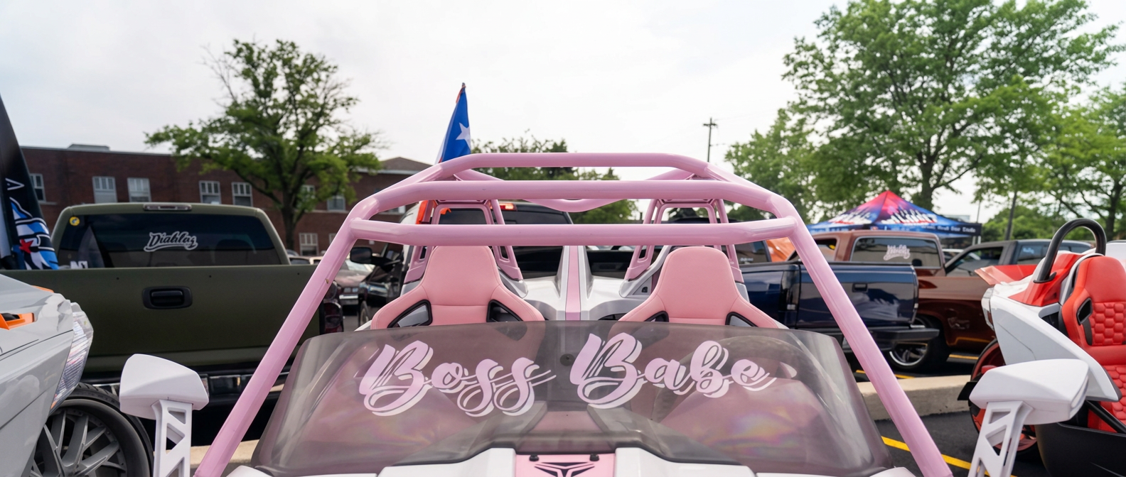 Pink and white Polaris Slingshot with a Boss Babe windshield decal and roll cage