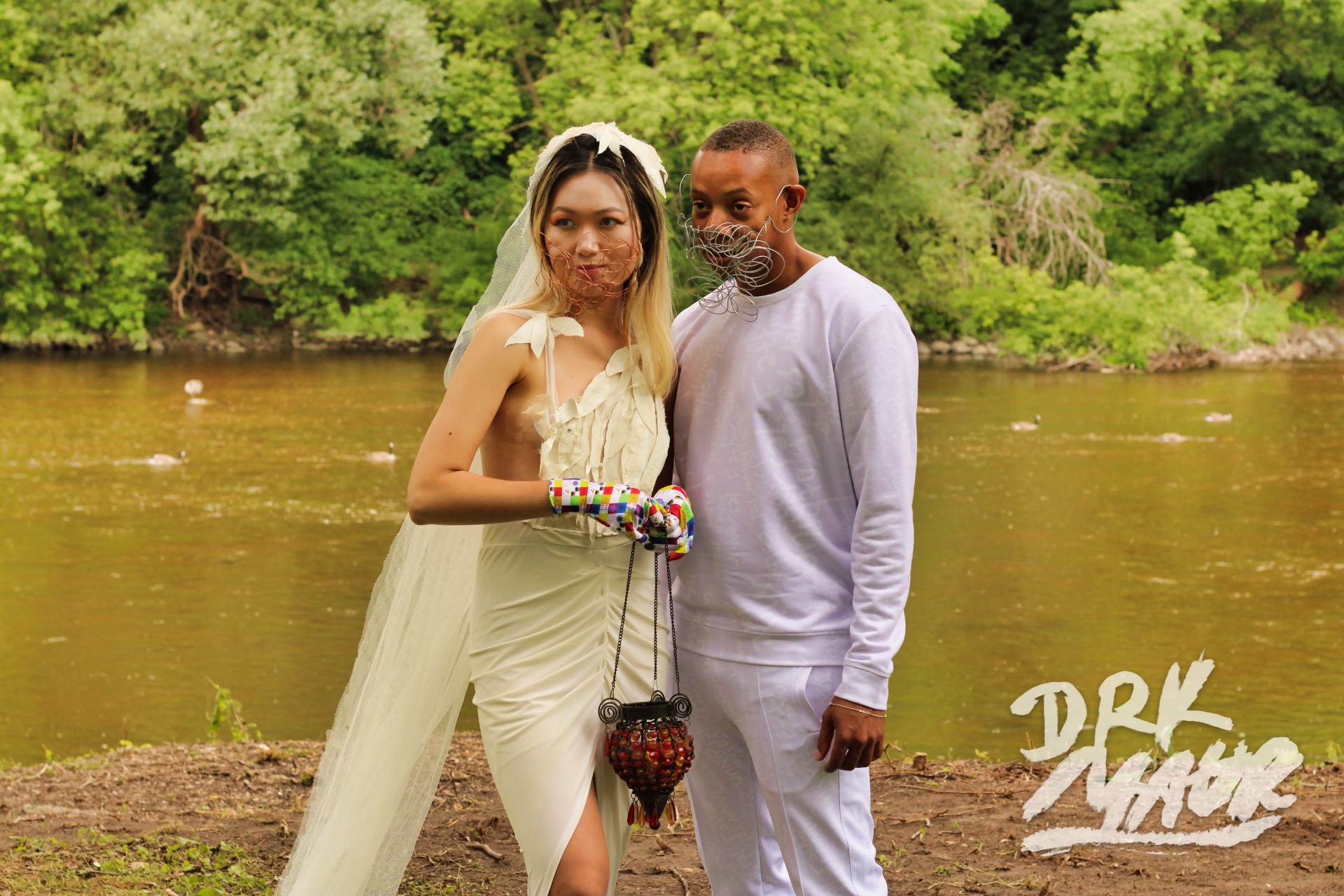 Two models in white couture and wire face pieces standing at a riverbank