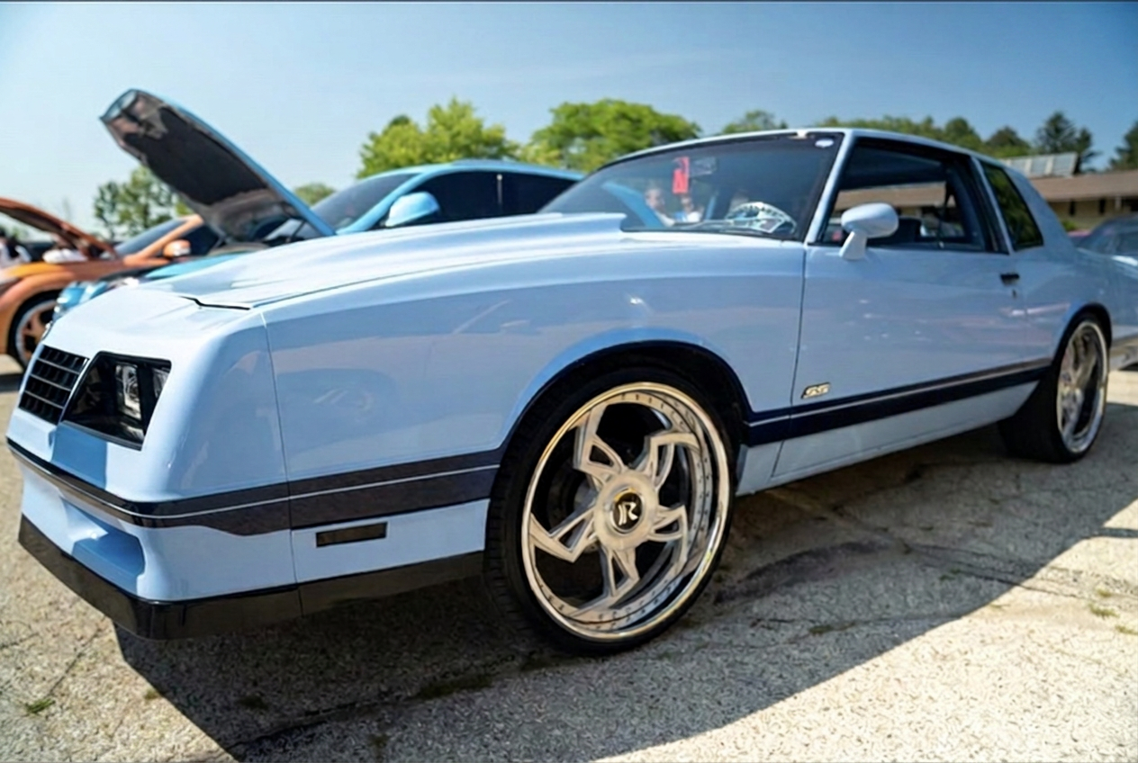 Powder blue Chevrolet Monte Carlo SS on gold and chrome wheels parked at an outdoor car show
