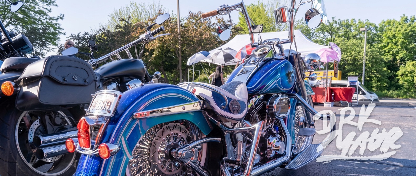Two custom baggers with ape hanger bars and blue metalflake paint parked side by side at an outdoor bike show