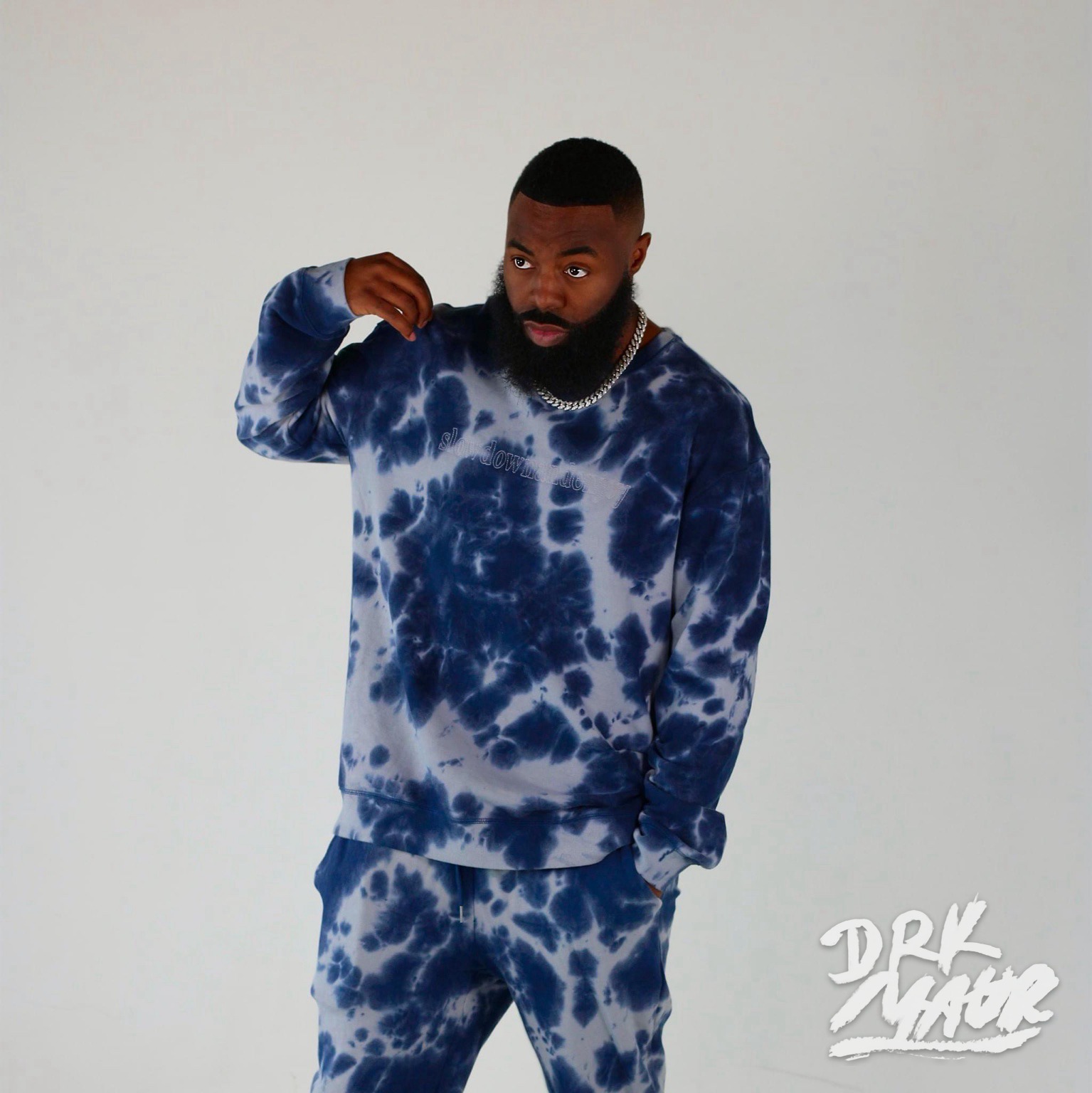 Studio fashion portrait of a bearded model in a navy and steel-blue tie-dye tracksuit embroidered with slow down world
