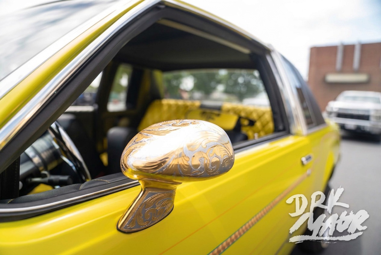 Gold engraved side mirror on a yellow lowrider with quilted interior visible through the window