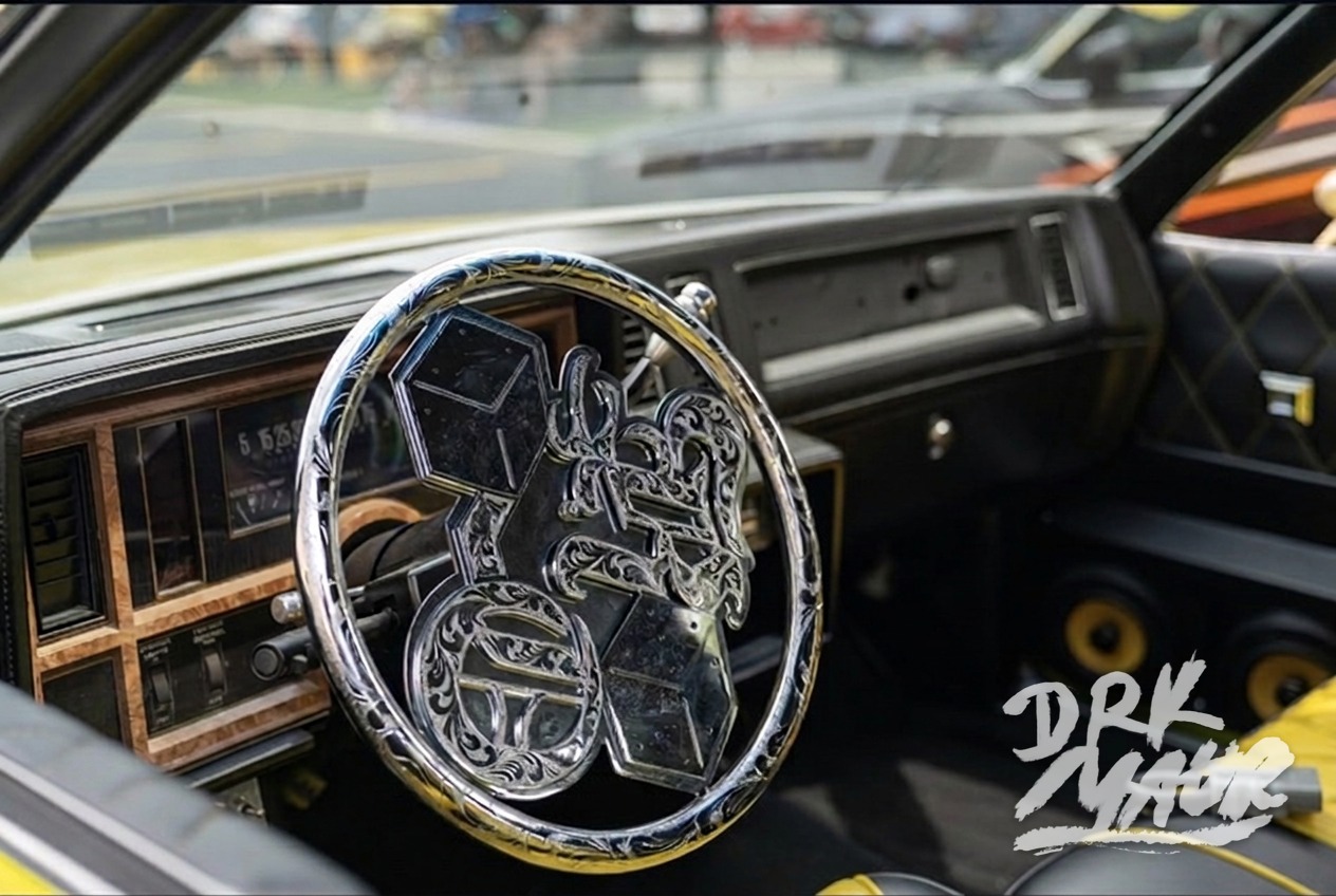 Engraved chrome custom steering wheel inside a yellow lowrider dashboard