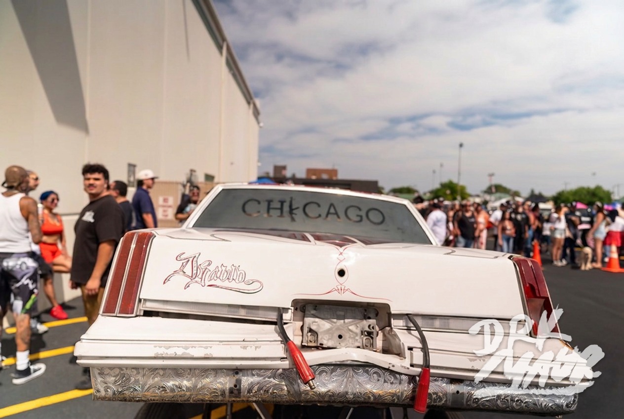 White lowrider hopping on hydraulics with its front end lifted high above the pavement at a car show