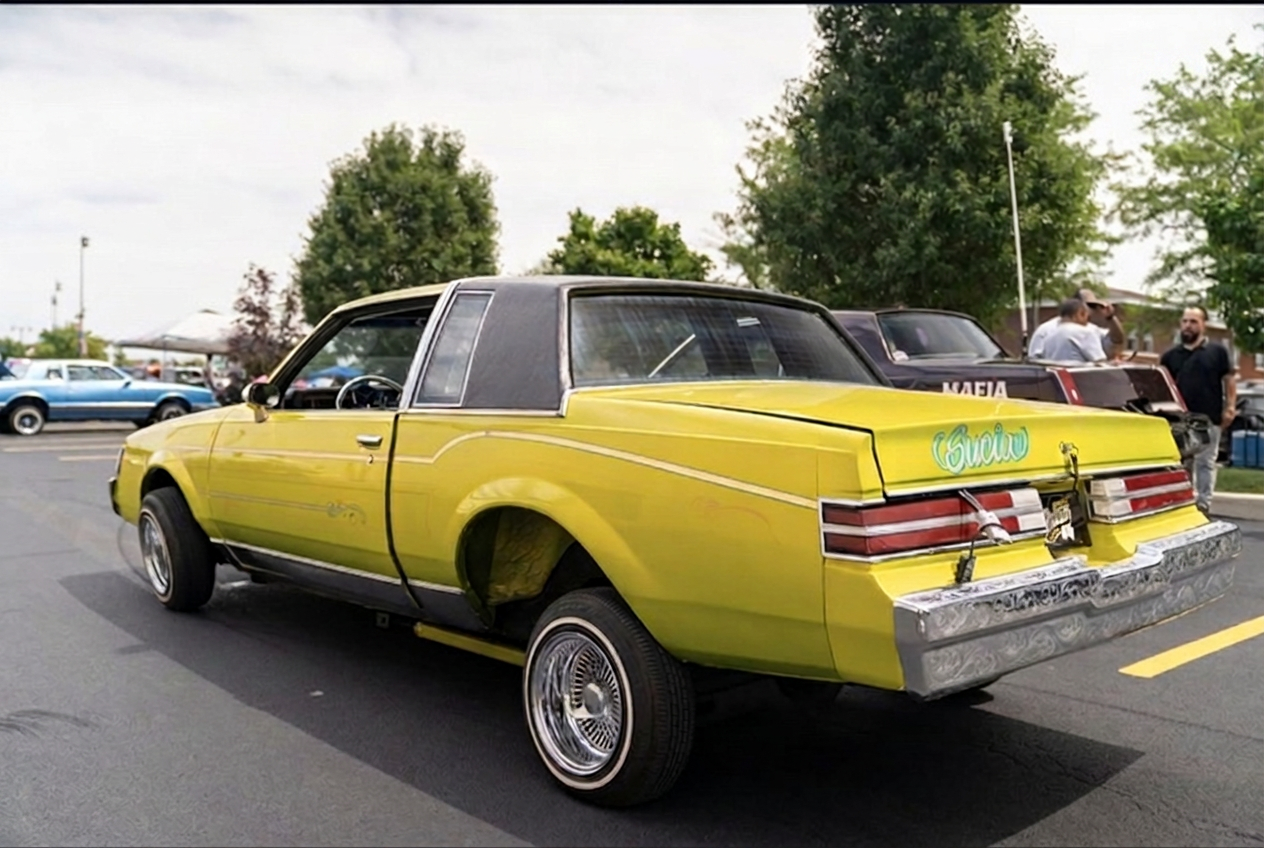 Yellow Buick Regal lowrider laid out on its rear bumper with engraved chrome trim