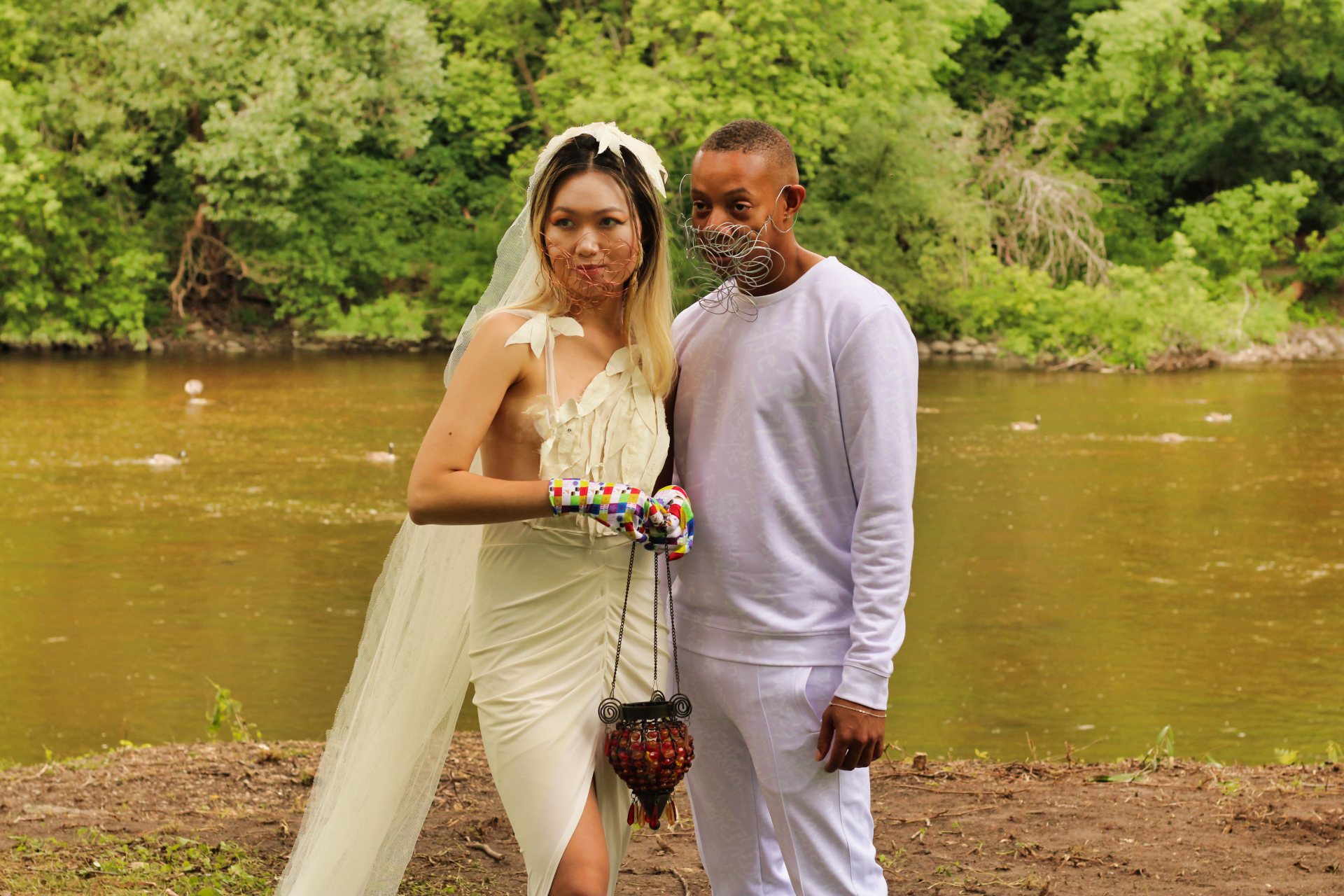 Two models in white couture and wire face pieces standing at a riverbank
