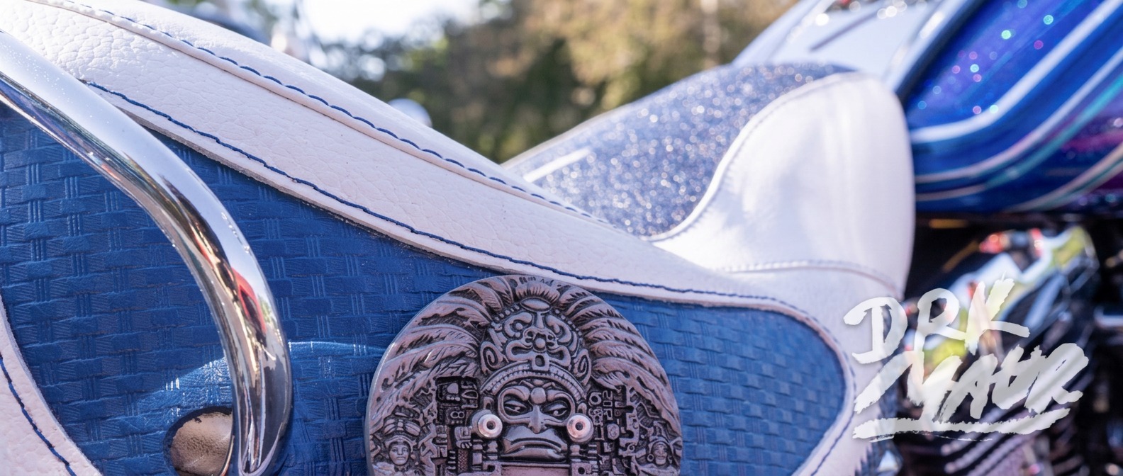 Close-up of a blue and white custom motorcycle seat with a tooled Aztec calendar medallion
