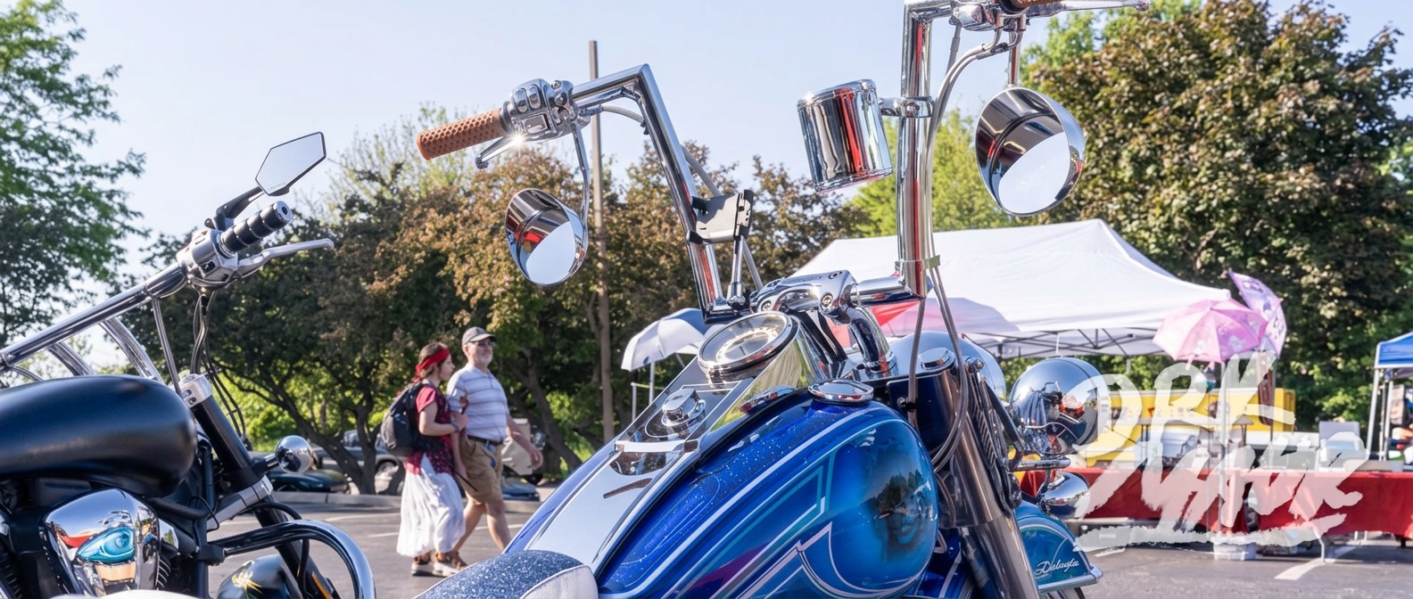 Blue metalflake custom bagger tank and chrome mirrors with show crowd walking past in the background