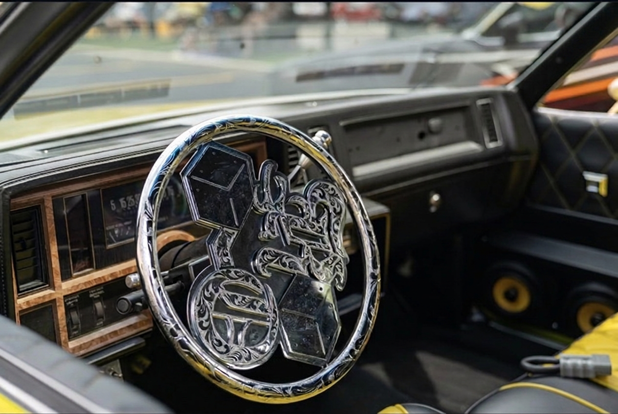 Engraved chrome custom steering wheel inside a yellow lowrider dashboard