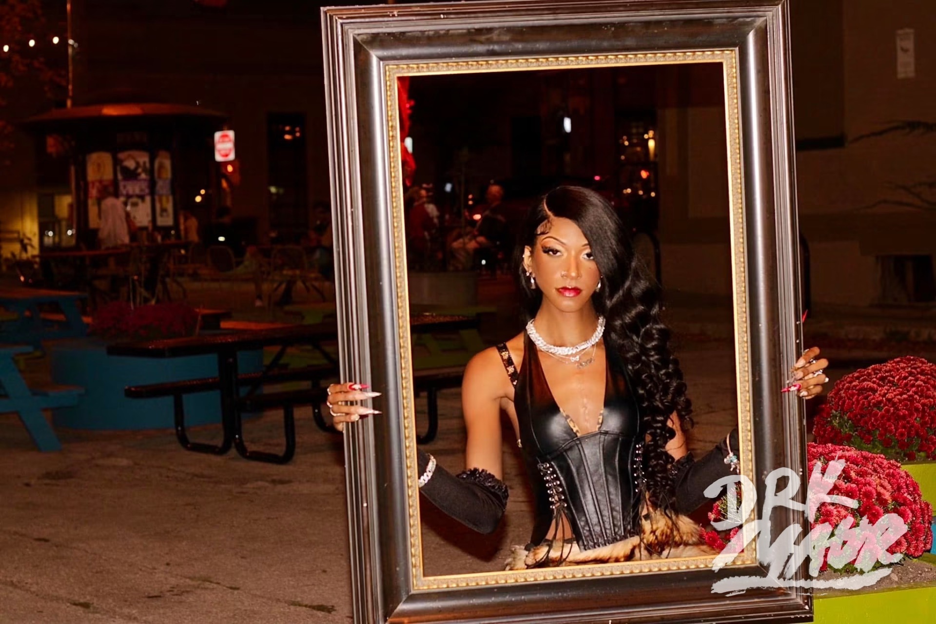 Model holding an empty gilded picture frame around herself on a patio at night
