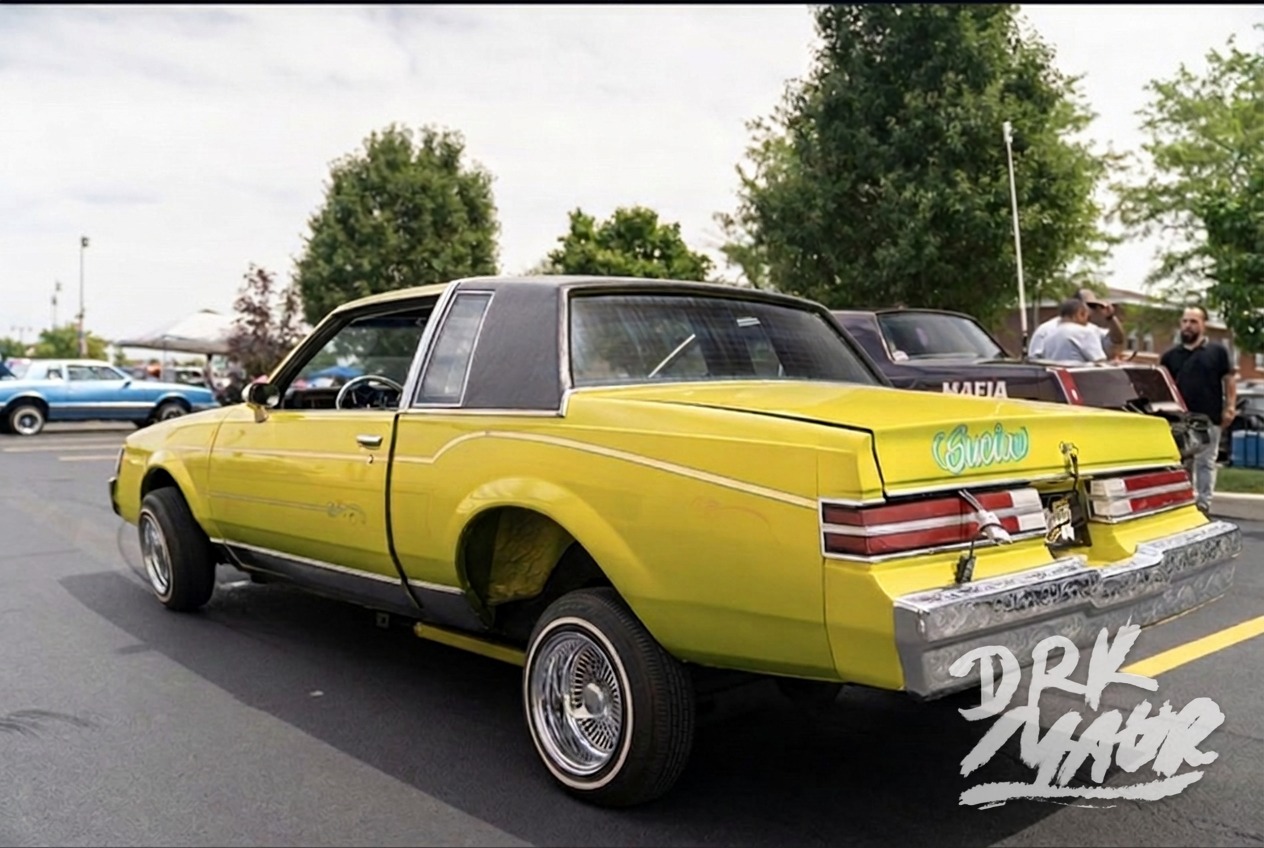 Yellow Buick Regal lowrider laid out on its rear bumper with engraved chrome trim