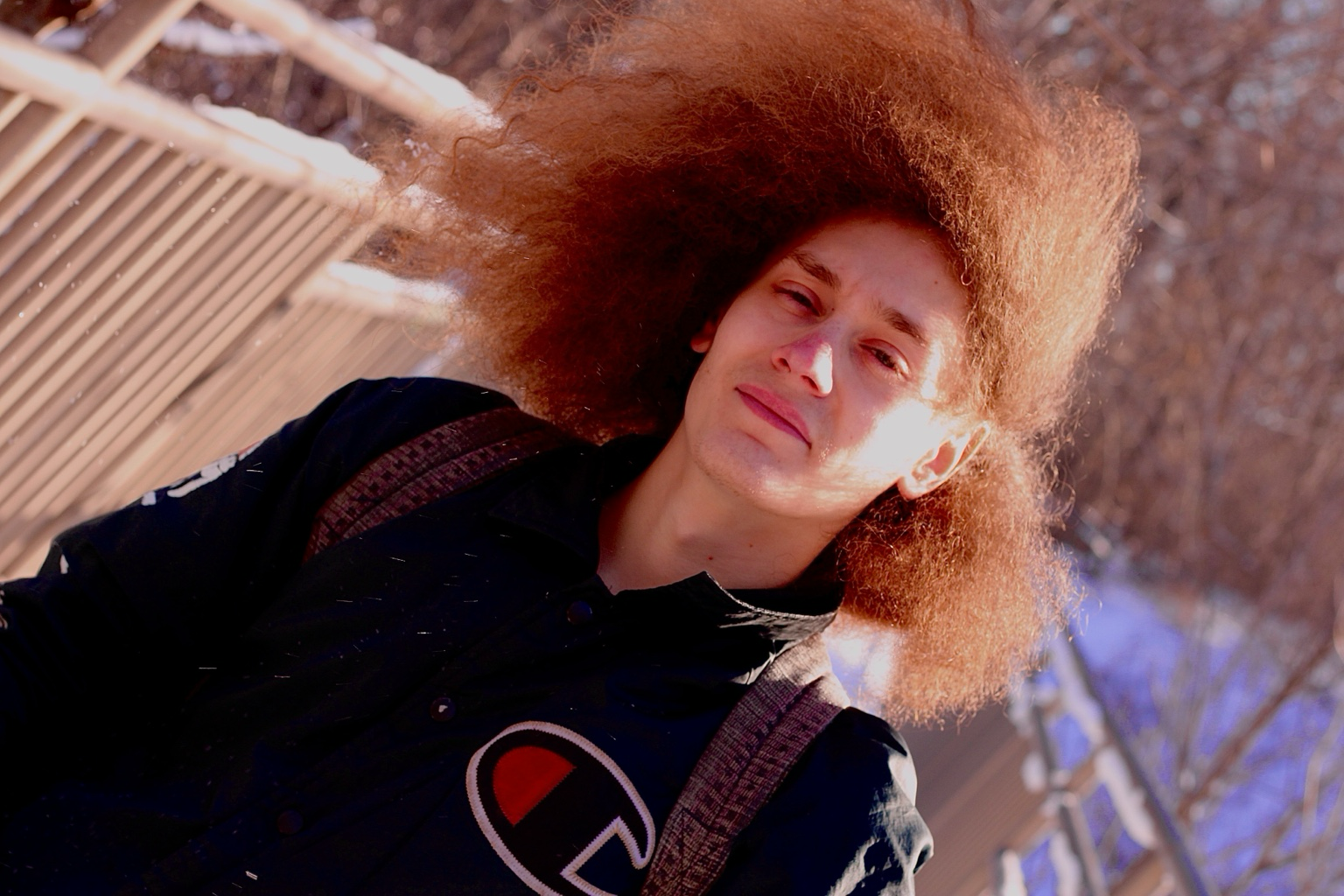 Outdoor portrait of a model with a voluminous reddish-brown afro in a navy Champion jacket against bare winter branches