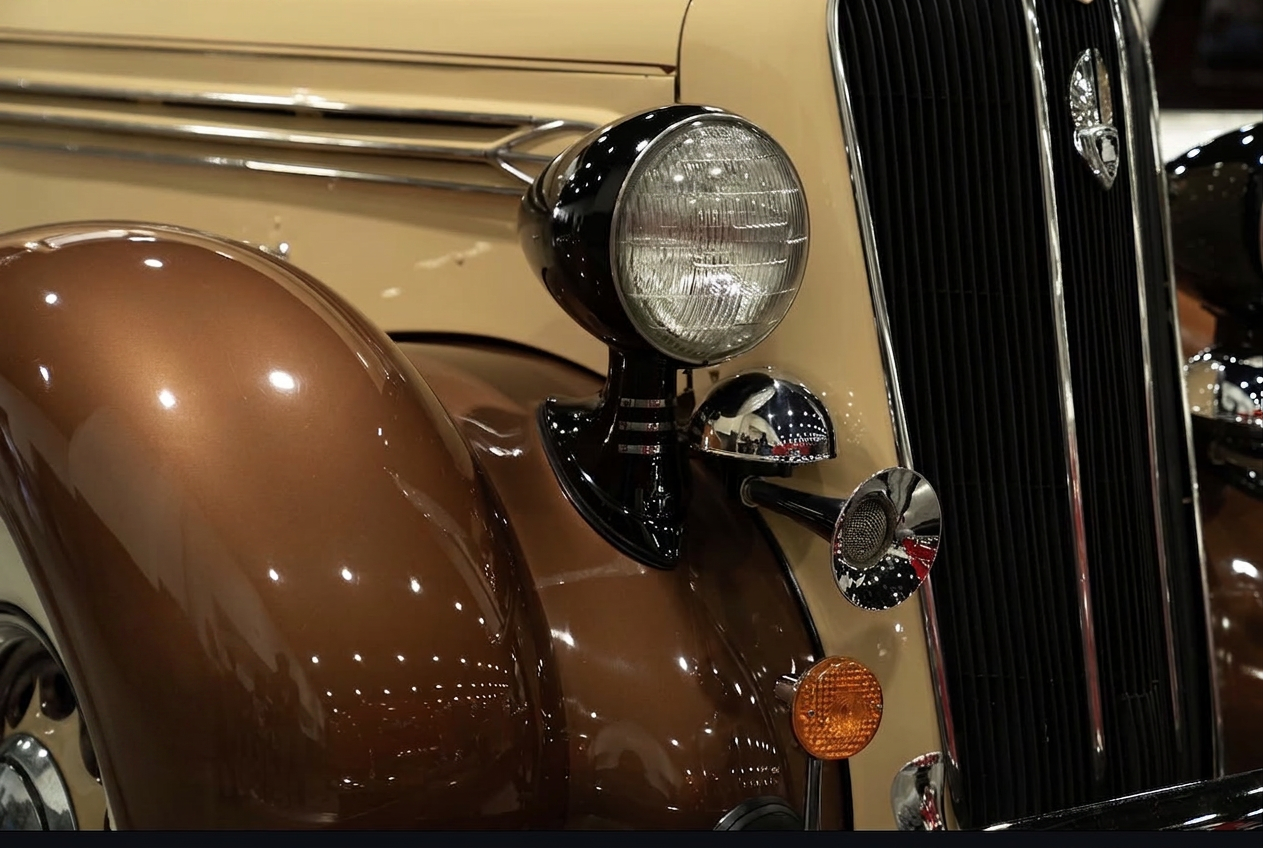 Close-up of a vintage Plymouth headlight, chrome grille and sweeping brown fender