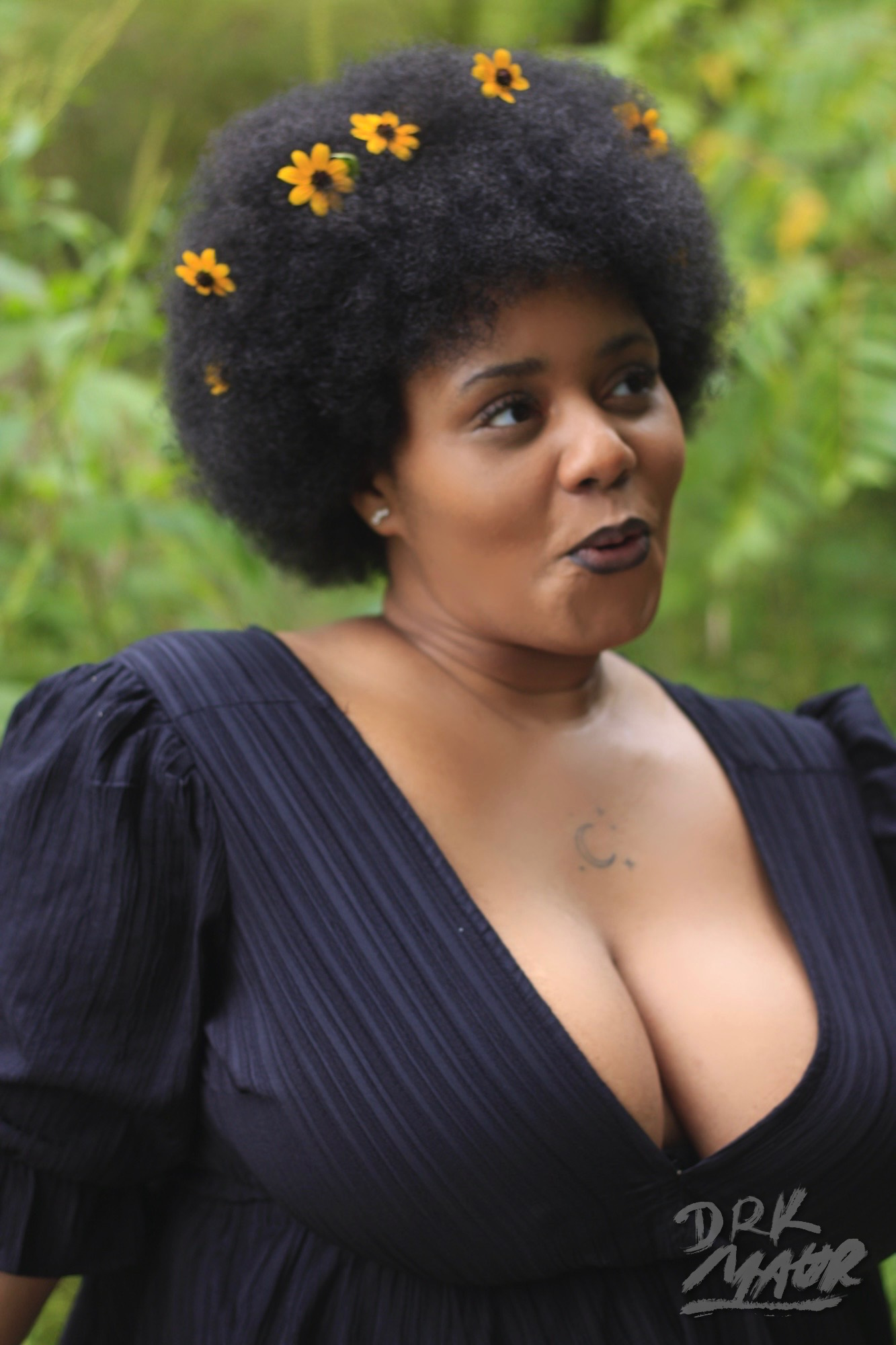 Candid close portrait of a smiling woman in a black dress with yellow flowers in her natural hair