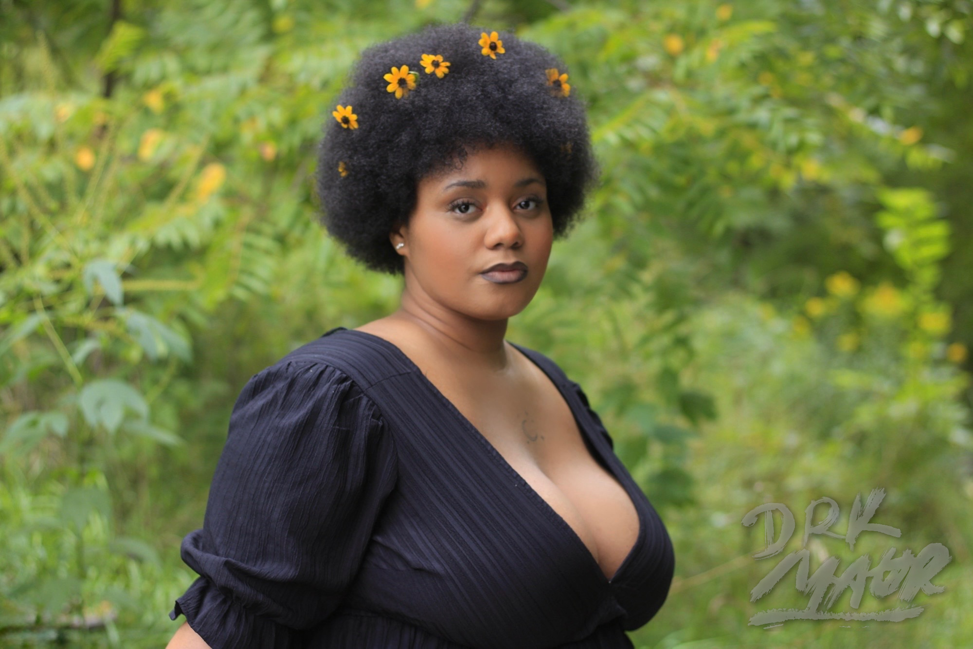 Environmental portrait of a woman in a black dress standing among lush green wildflowers