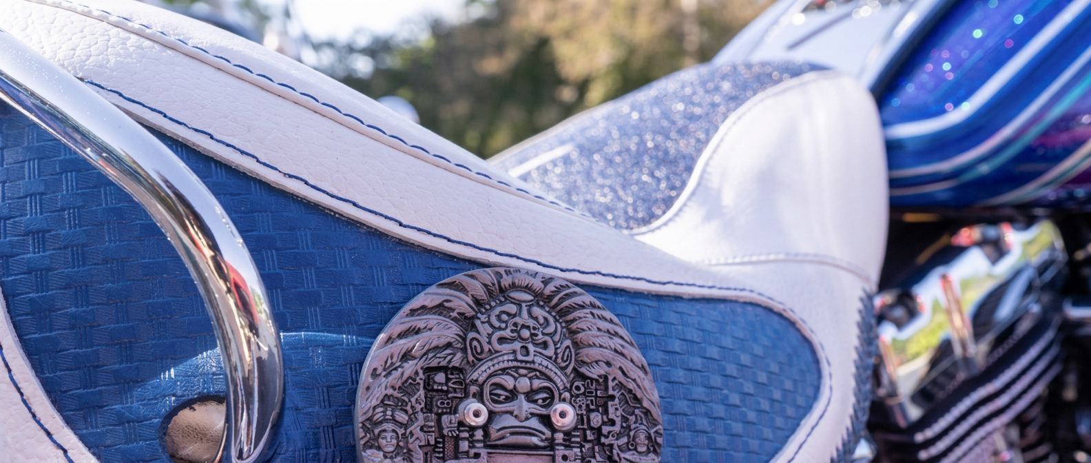 Close-up of a blue and white custom motorcycle seat with a tooled Aztec calendar medallion