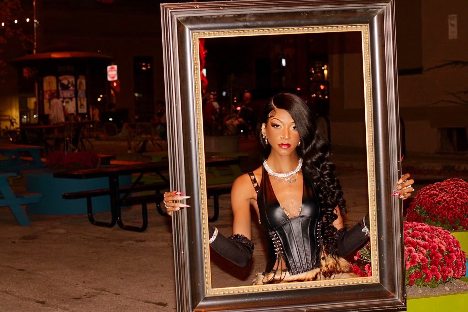 Model holding an empty gilded picture frame around herself on a patio at night