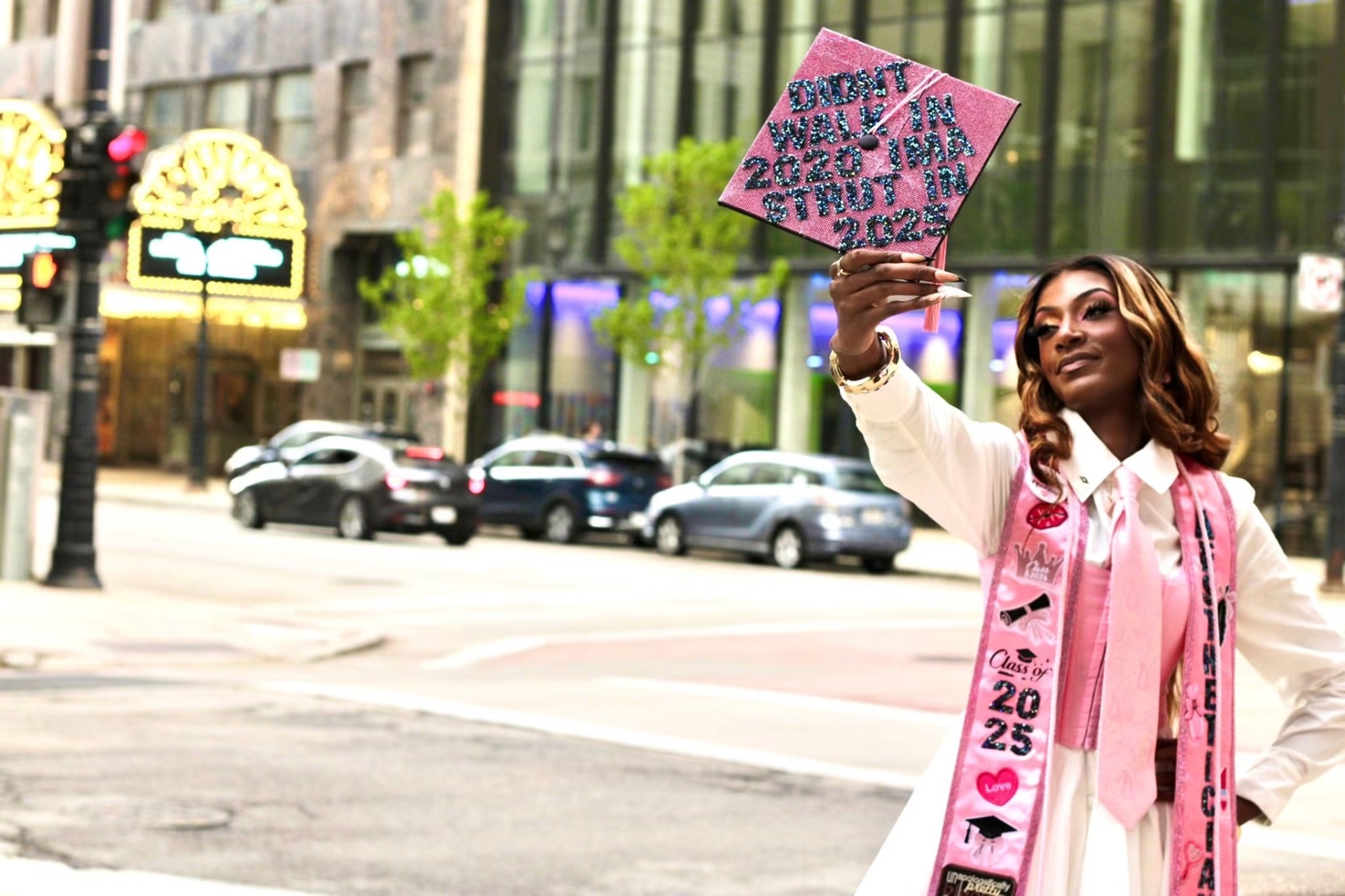 Graduate raising her rhinestone graduation cap above her head on a city street