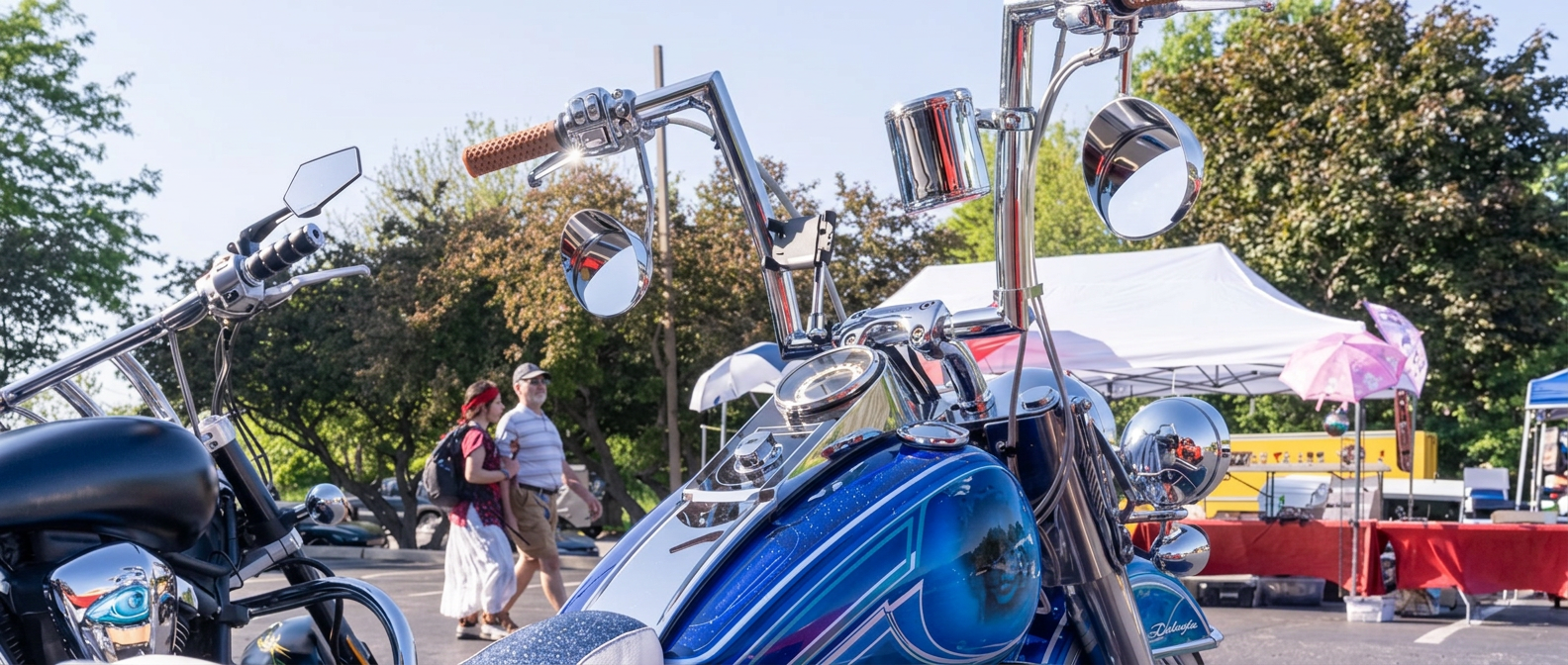 Blue metalflake custom bagger tank and chrome mirrors with show crowd walking past in the background