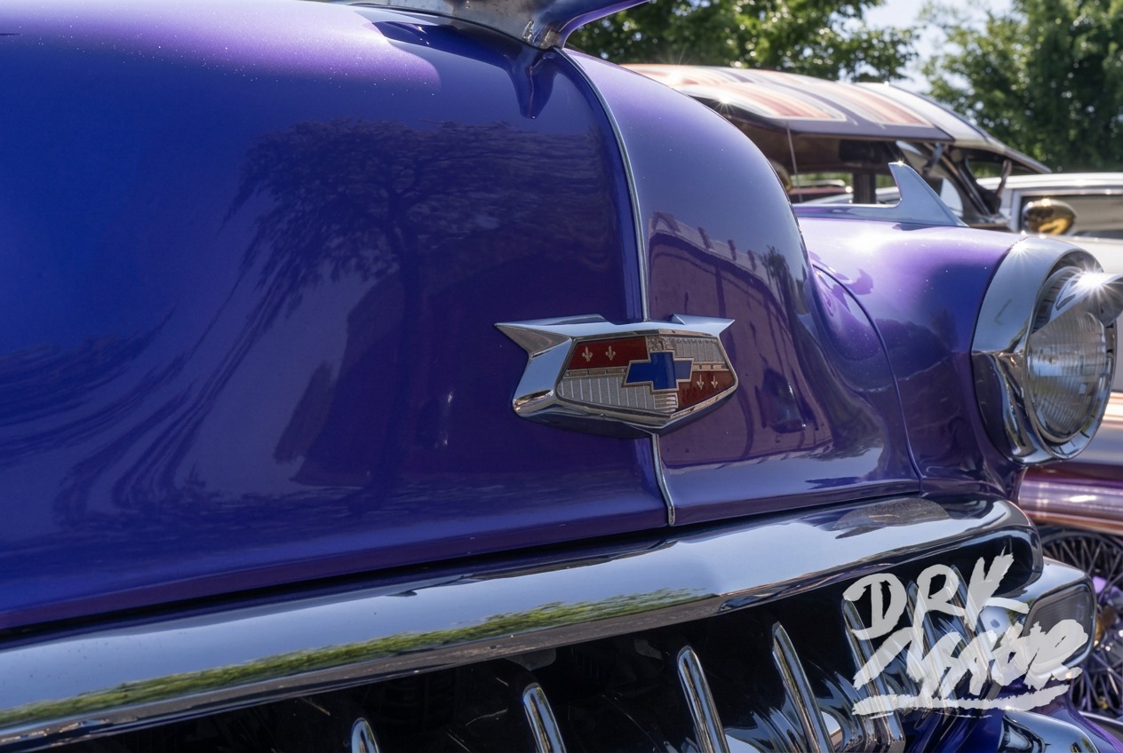 Chrome Chevrolet crest emblem on the deep purple hood of a customized classic Chevy at a car show