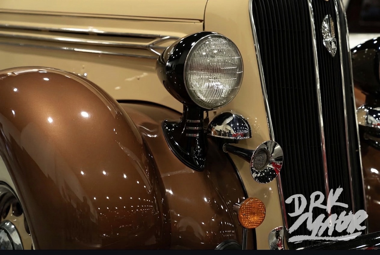 Close-up of a vintage Plymouth headlight, chrome grille and sweeping brown fender