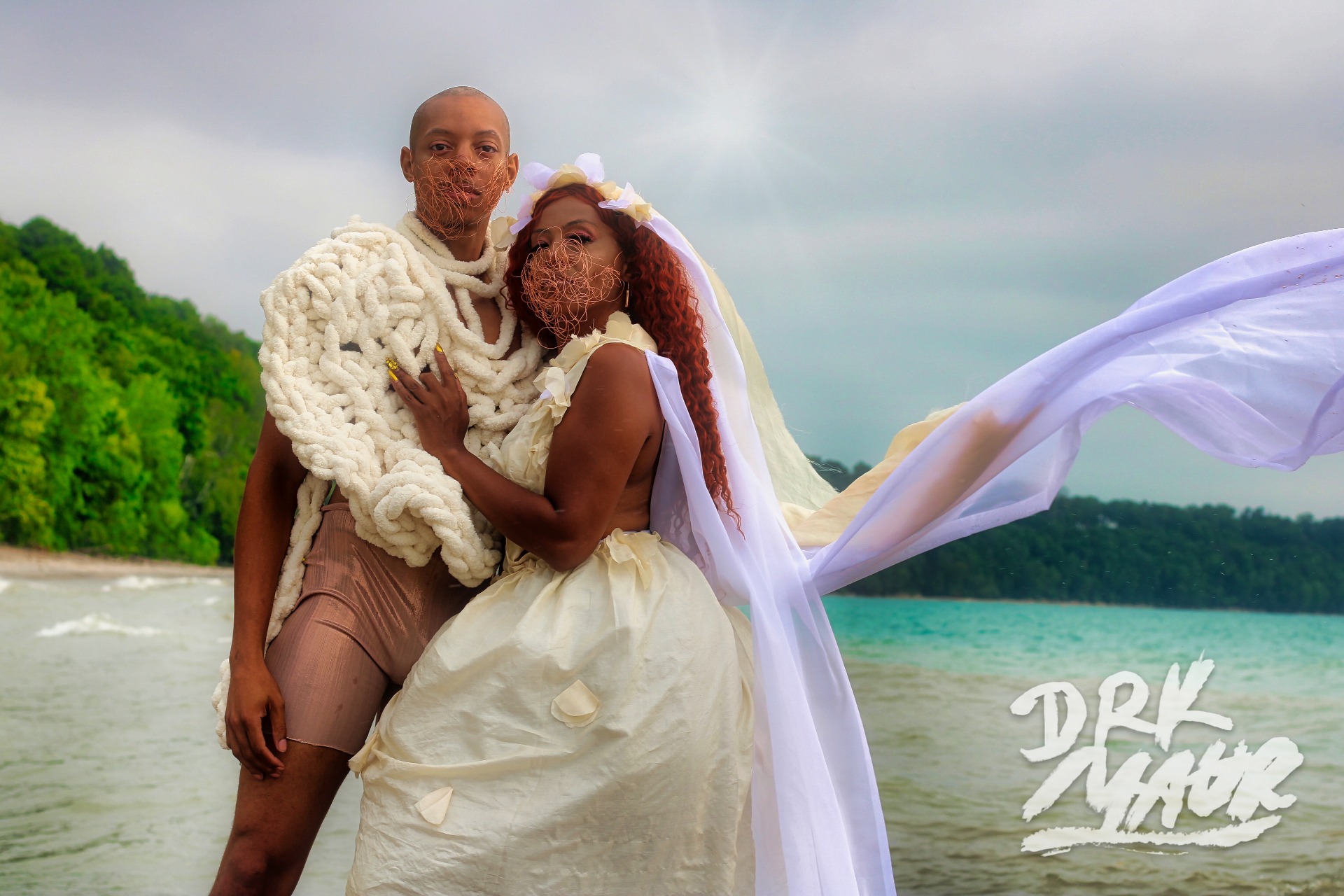 Two models in handmade white garments with veils blowing in the wind on a lakeshore