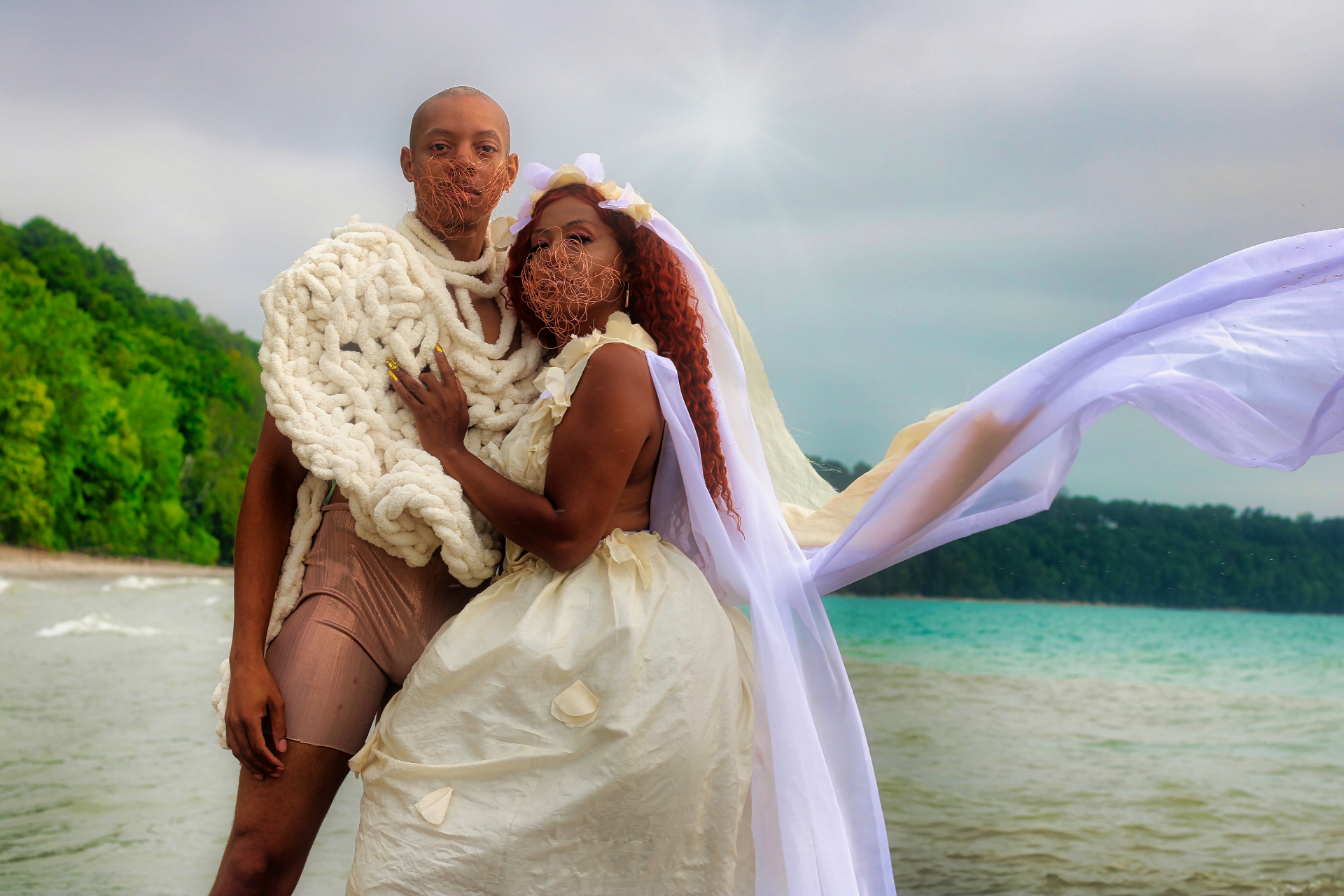 Two models in handmade white garments with veils blowing in the wind on a lakeshore
